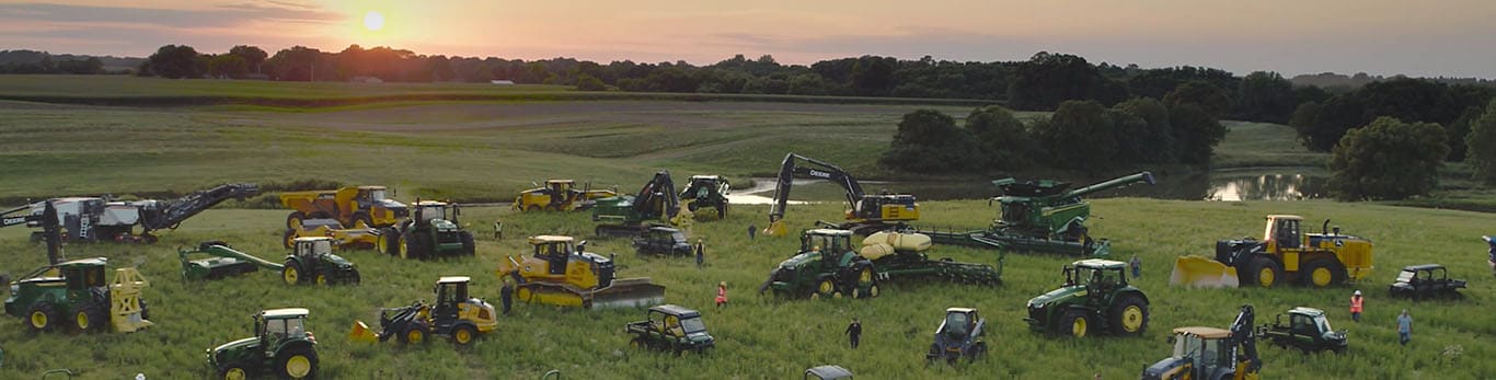 Люди йдуть великим полем серед різноманітного обладнання марки John Deere.