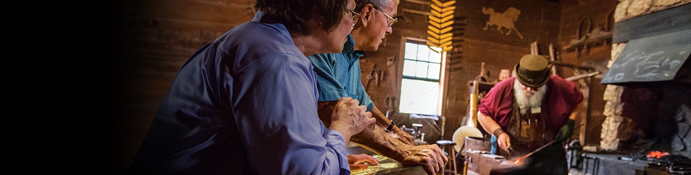Пожилая пара смотрит на кузнеца с металлическим молотом на историческом участке в Гранд-Детур, Иллинойс, США
