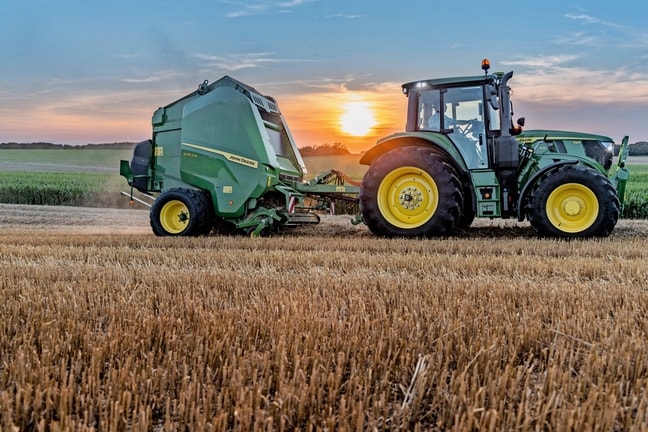 John Deere V462M на полі соломи, який буксирується John Deere 6M 150 на заході сонця