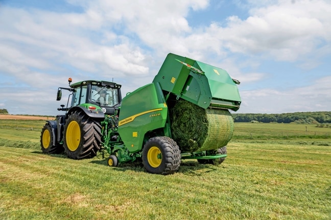 Прес-підбирач John Deere F442M, який буксирується трактором John Deere 6M, що виштовхує тюк трави