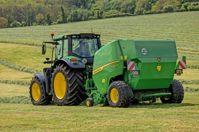 Прес-підбирач John Deere F442M, який буксирується трактором 6M John Deere на горбистому полі трави