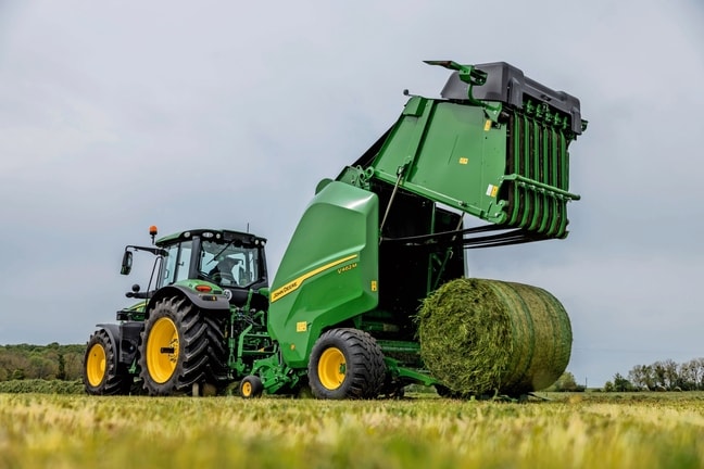 Прес-підбирач John Deere V462M, який буксирується трактором John Deere 6M, що виштовхує тюк трави